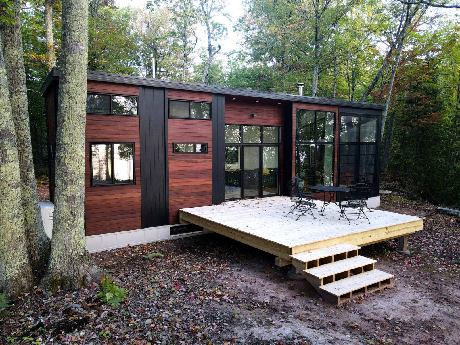 Modern tiny home with large windows and a spacious front porch in a forest setting